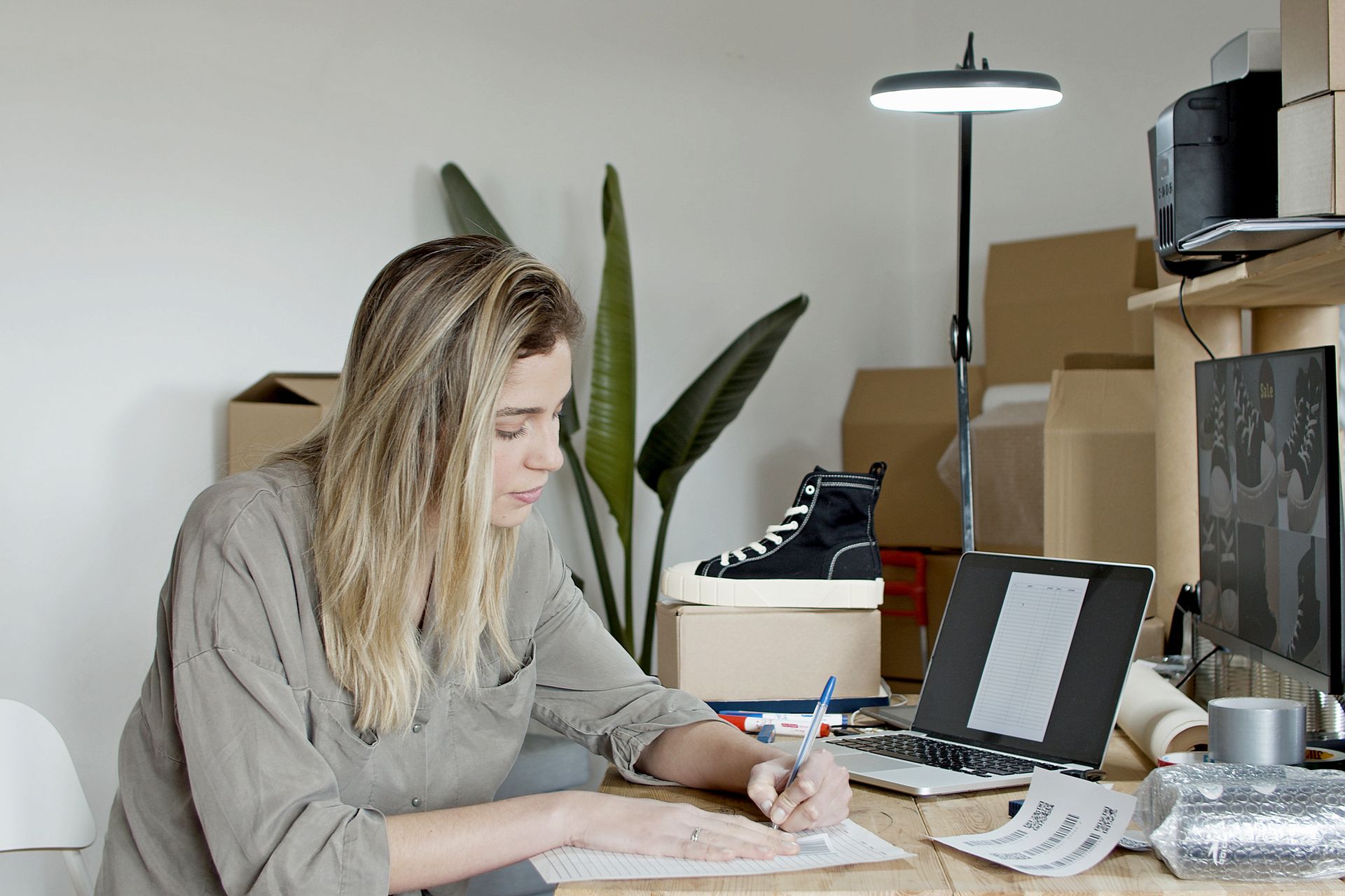 Businesswoman writing notes in a busy online store office in Portugal, focusing on growth and efficiency.