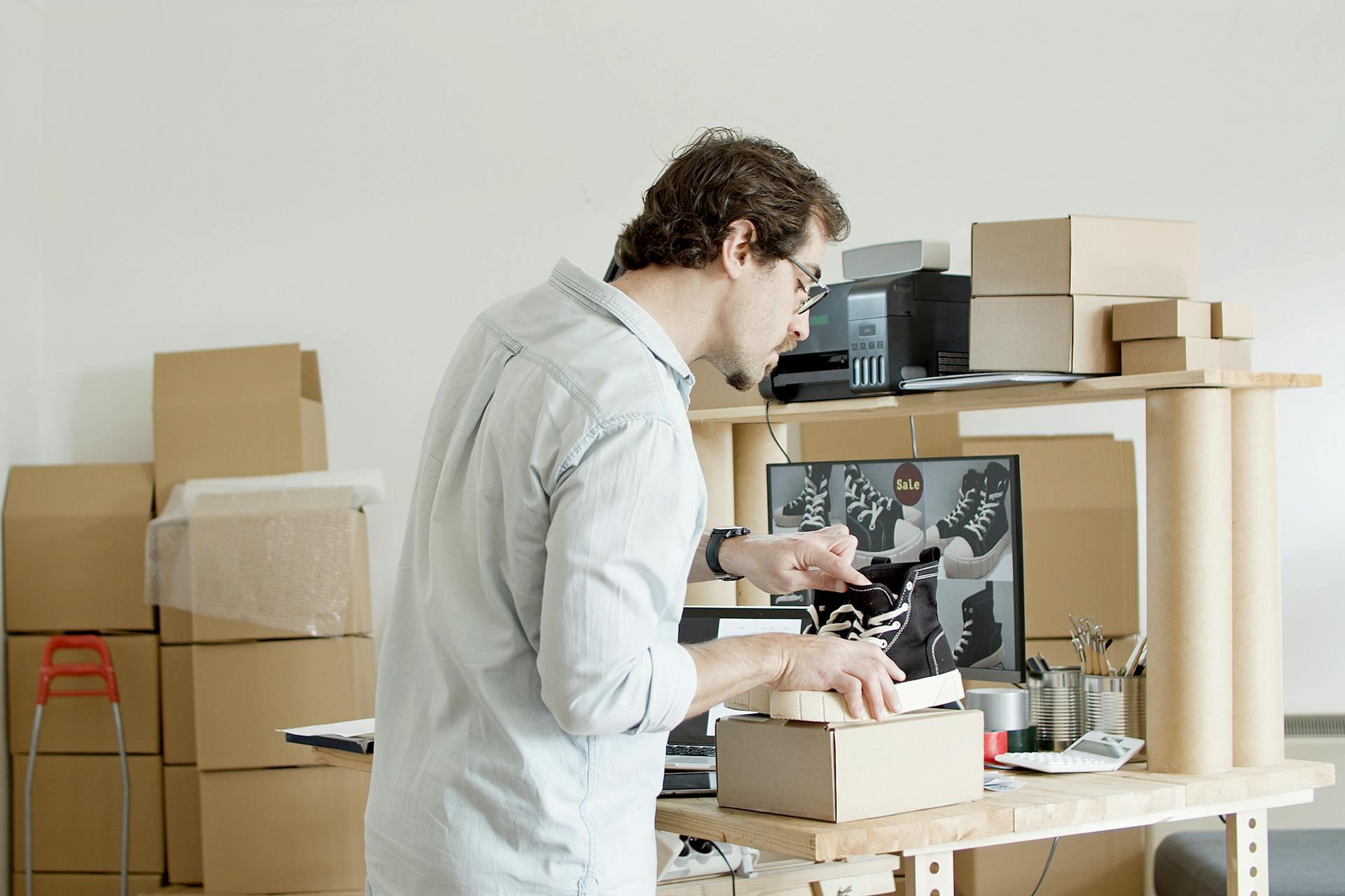 A businessman working in an online store packing shoes in a cardboard box.