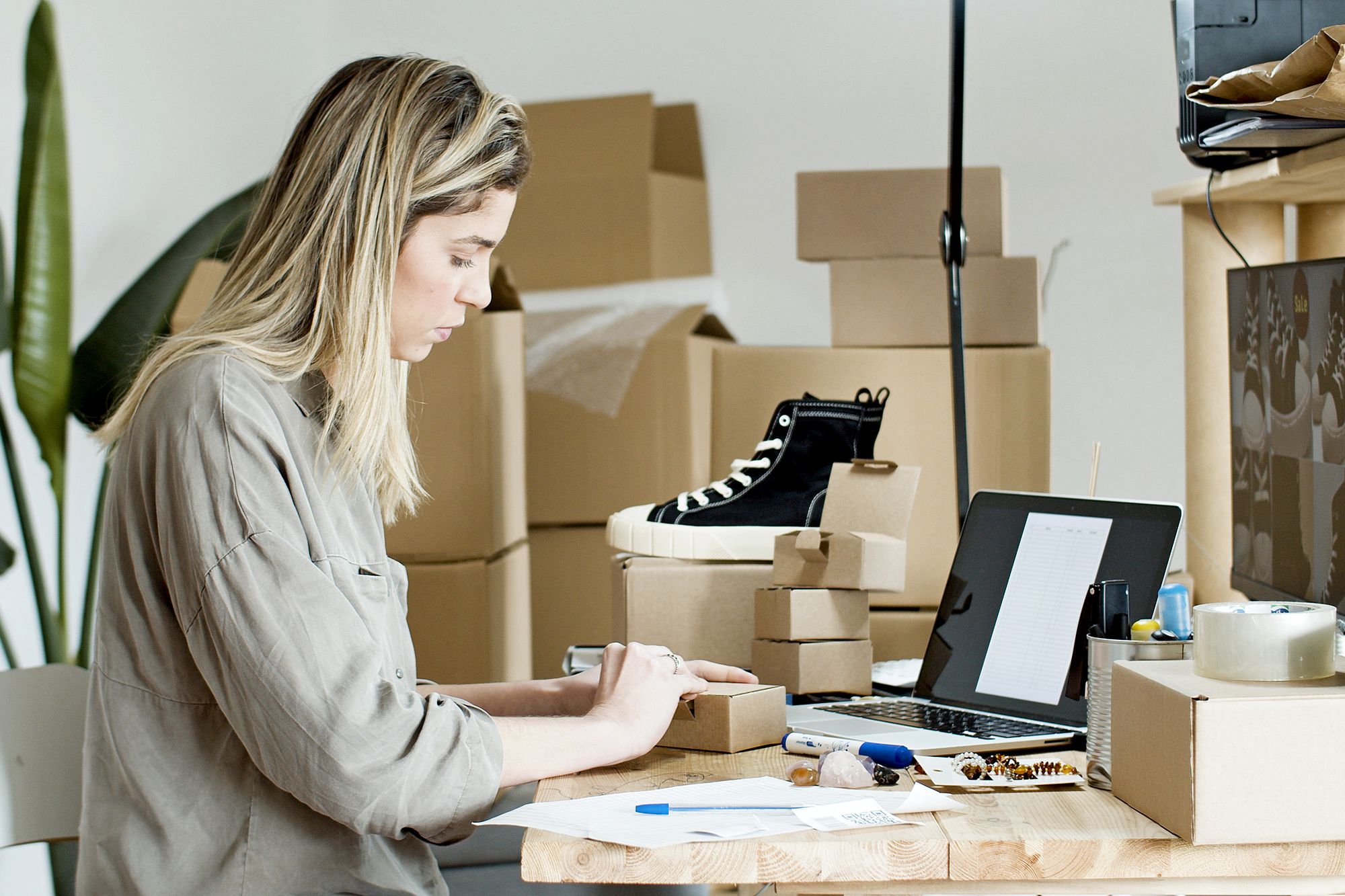 Persona empaca cajas de productos junto a una laptop en un pequeño taller