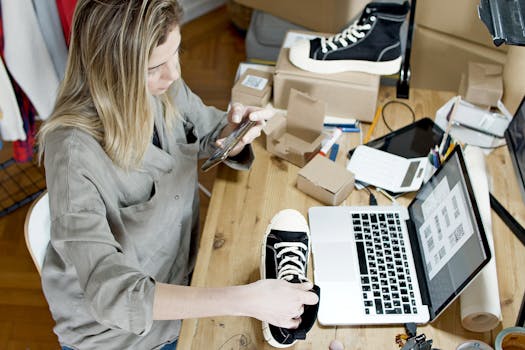 Small business owner international shipping - Woman photographing shoes for online sale in home workspace with laptop and packages.