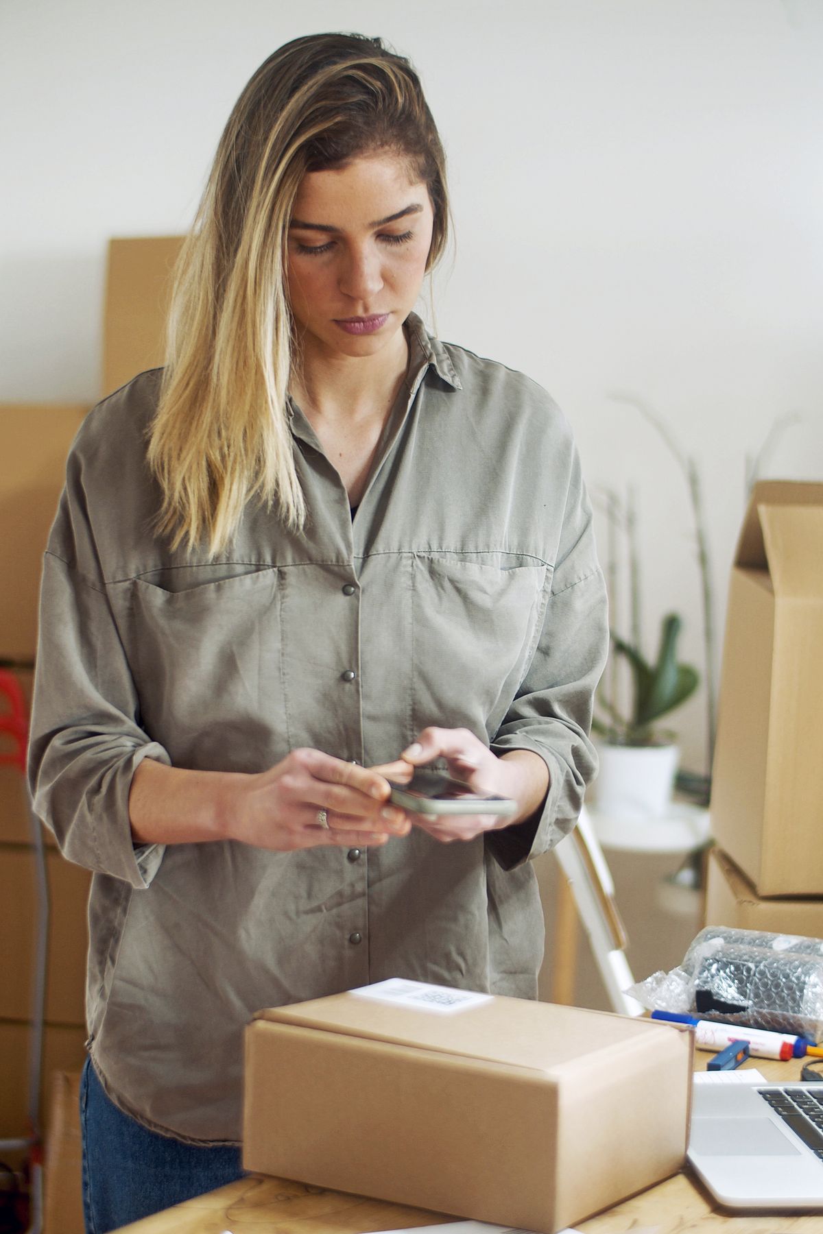 Online seller using a smartphone while preparing customer packages