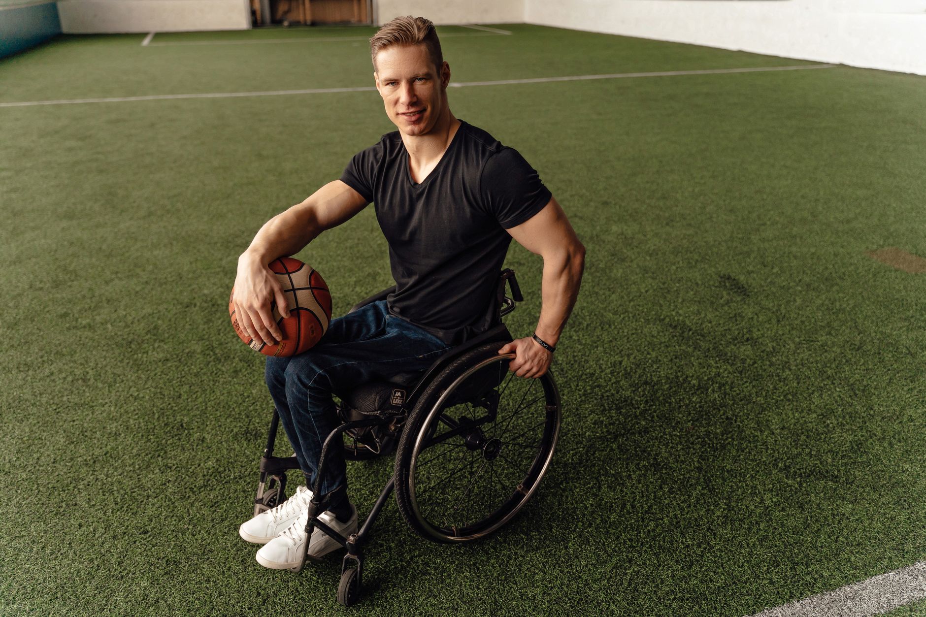 Man in a wheelchair holding a basketball on an indoor sports court, showcasing inclusivity in sports.