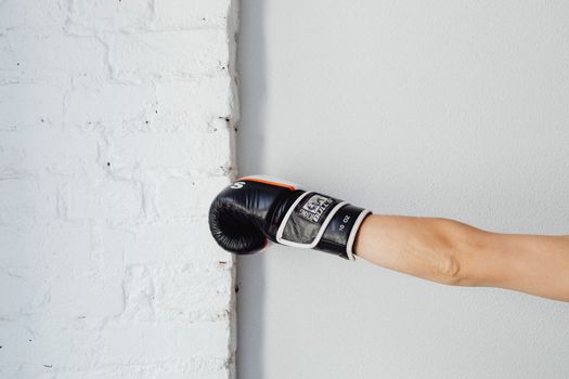 A boxing glove worn by a person punching a white brick wall, indoors with natural lighting.