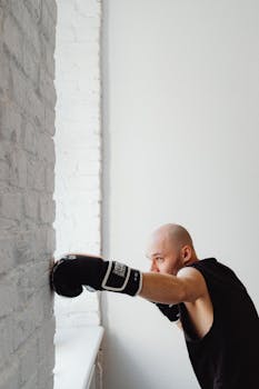Bald male boxer practicing punches against a white brick wall indoors.