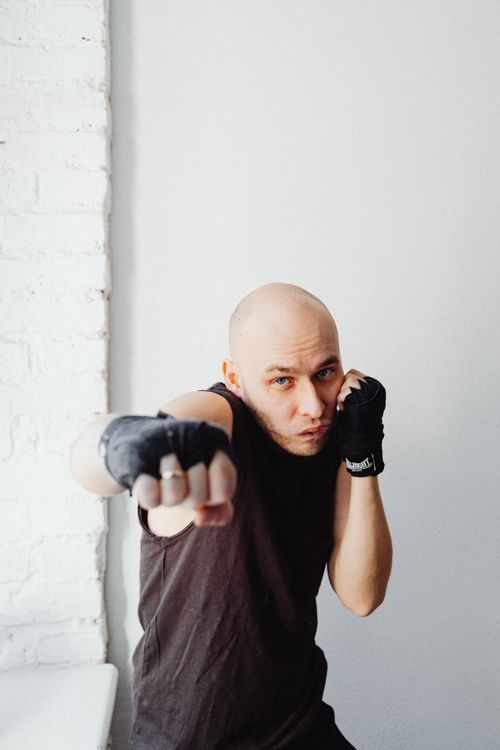 Free Bald male boxer in a black tank top practicing punching indoors with hand wraps on. Stock Photo