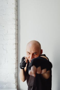 Focus on a bald male boxer in a fighting stance, throwing a punch indoors.