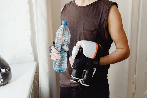 Free A male boxer holding a water bottle and boxing gloves, representing a healthy lifestyle. Stock Photo