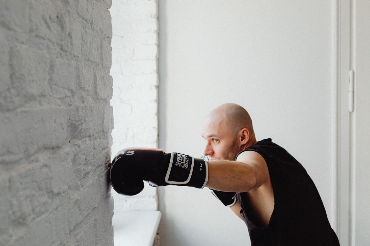 bald man practicing boxing against a brick wall indoors focusing on fi