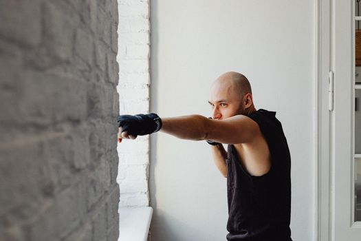 Bald man working out indoors, practicing boxing in a combat sport routine.