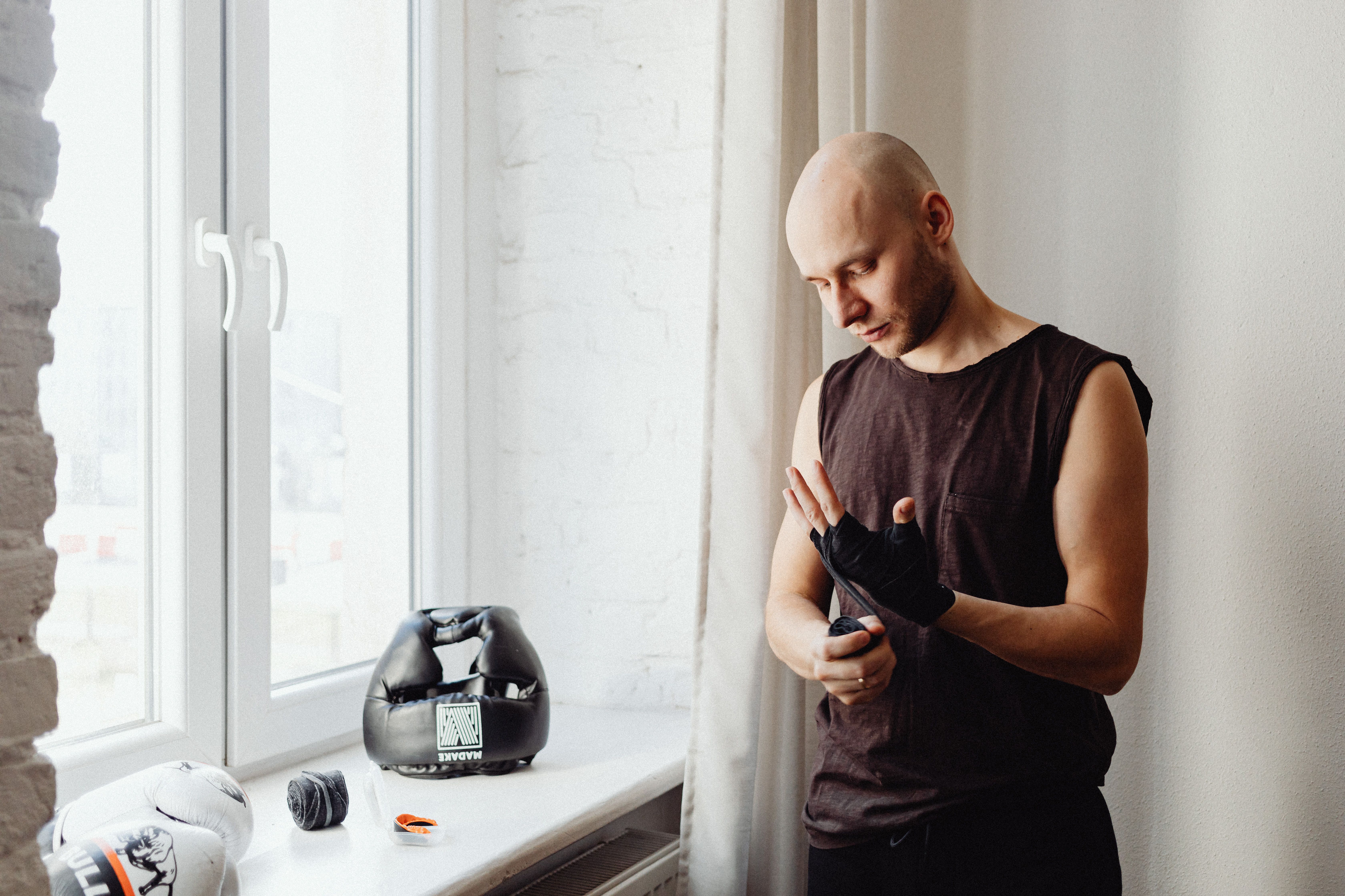 A Man Wrapping His Hand while Standing Near the Window · Free Stock Photo