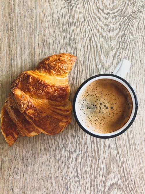 Free A crispy croissant paired with a steaming cup of coffee on a rustic wooden table. Stock Photo