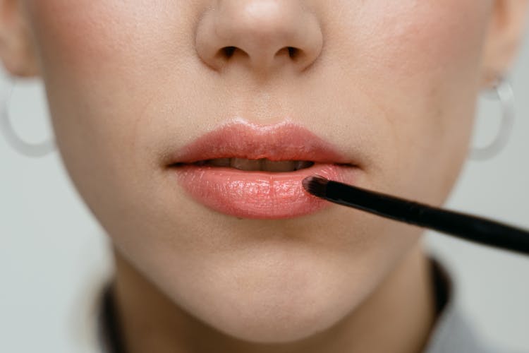 A Woman Applying Lipstick With A Lip Brush