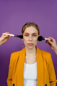 Stylish portrait of a woman with makeup brushes against a bold purple background.