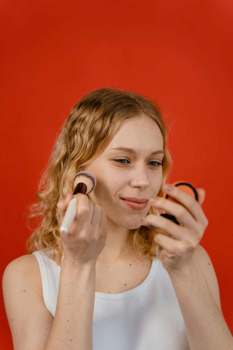 A Woman Applying Makeup On Her Face While Looking At The Mirror