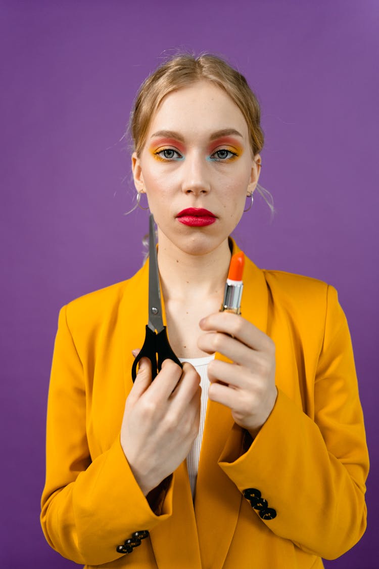 Woman In Yellow Blazer Holding Lipstick And Scissors