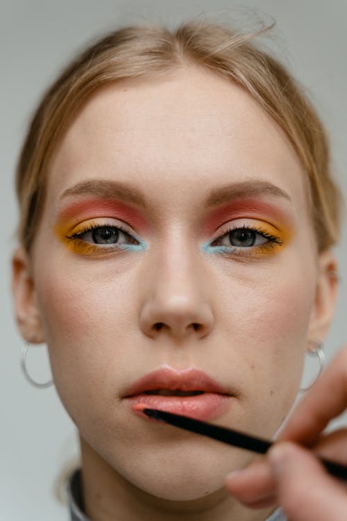 A Woman in Colorful Eyeshadow Looking while Applying Lipstick