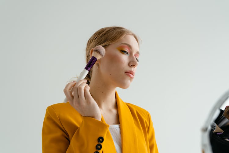 A Woman In Yellow Blazer Holding Makeup Brush