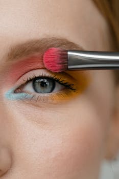 Vibrant eye makeup being applied with a brush, featuring red, yellow, and blue tones.