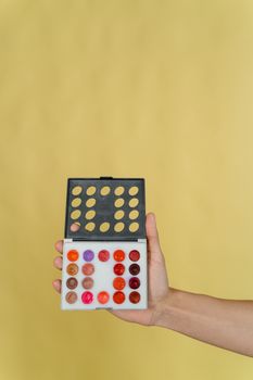 A hand holding a vibrant makeup palette against a yellow background, showcasing various lip shades.