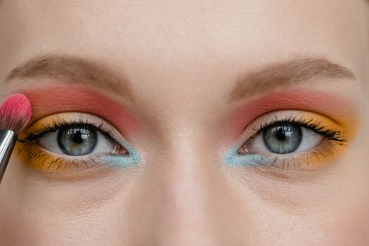 Close-up of eyes with vibrant multicolored eyeshadow and a makeup brush.