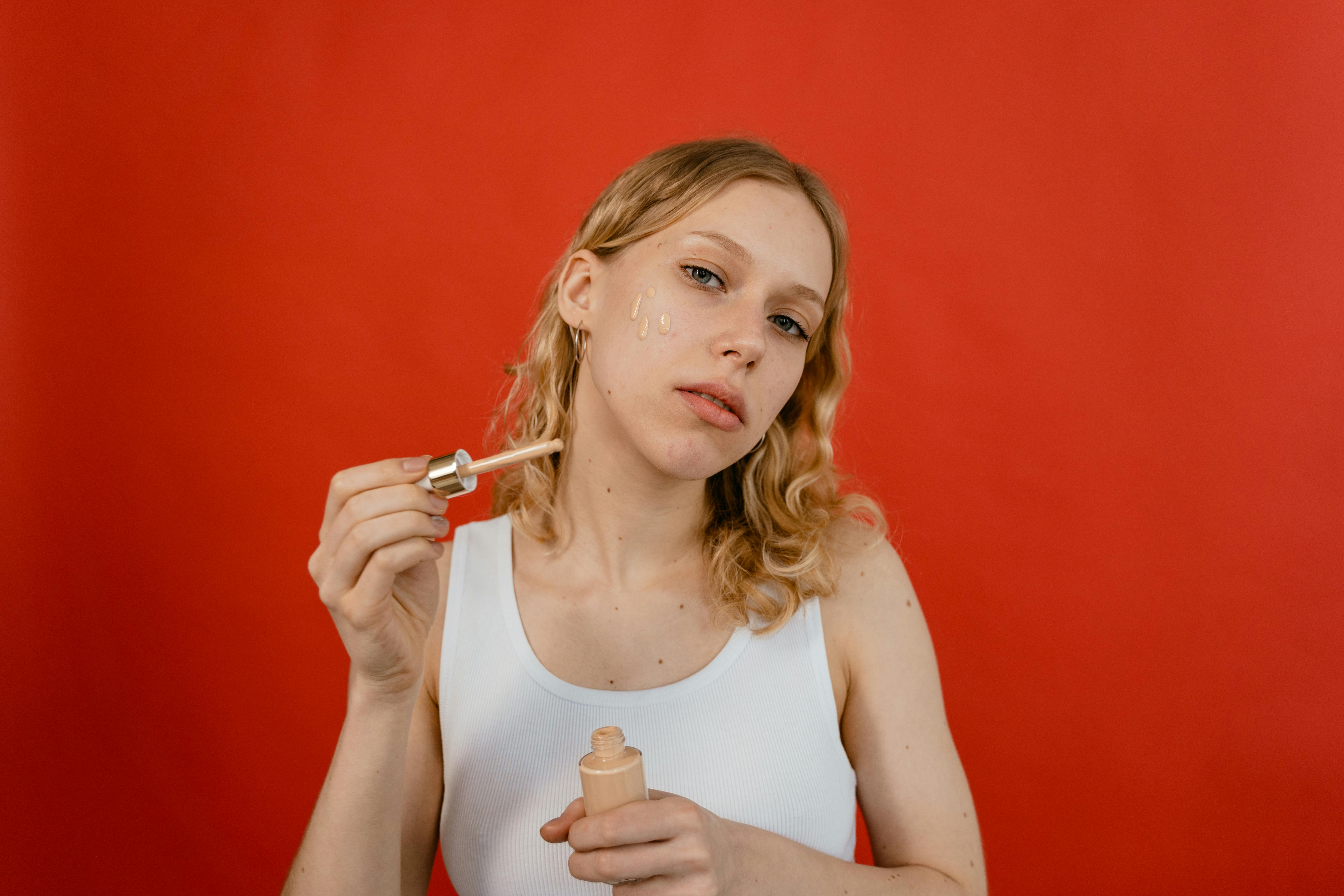 woman in white tank top holding glass container with brown cream