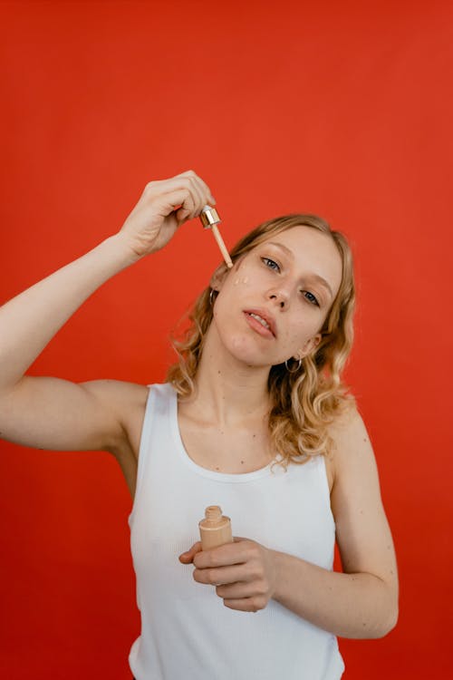 A Woman in White Tank Top Applying a Concealer on Her Face