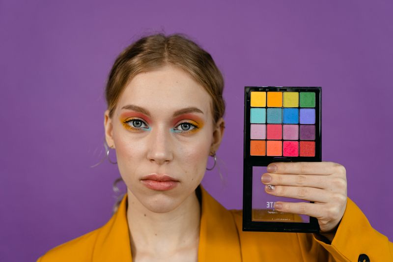 Woman showcasing colorful eye makeup and palette on a purple background.