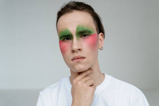 Portrait of a man wearing vibrant green and red makeup, expressing creativity indoors.