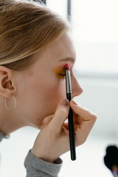 A close-up image of a young woman applying eye shadow with a brush.