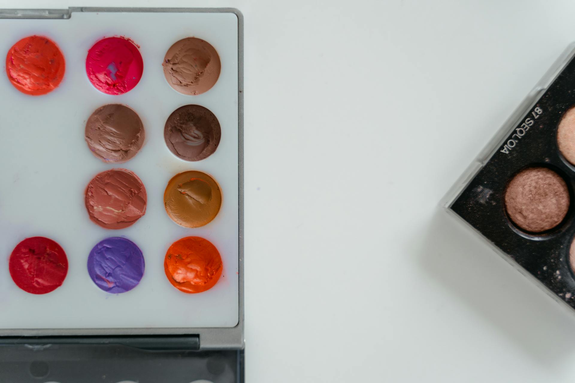A colorful array of eyeshadow and cosmetic palette arranged in an artistic flat lay.