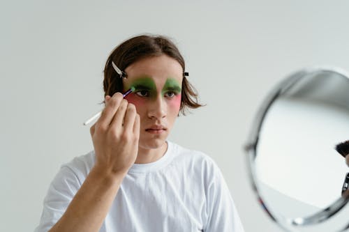 A Man Applying Makeup while Looking at a Mirror