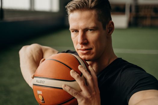 Portrait of a determined basketball player holding a ball indoors, showcasing intense focus and athletic strength.