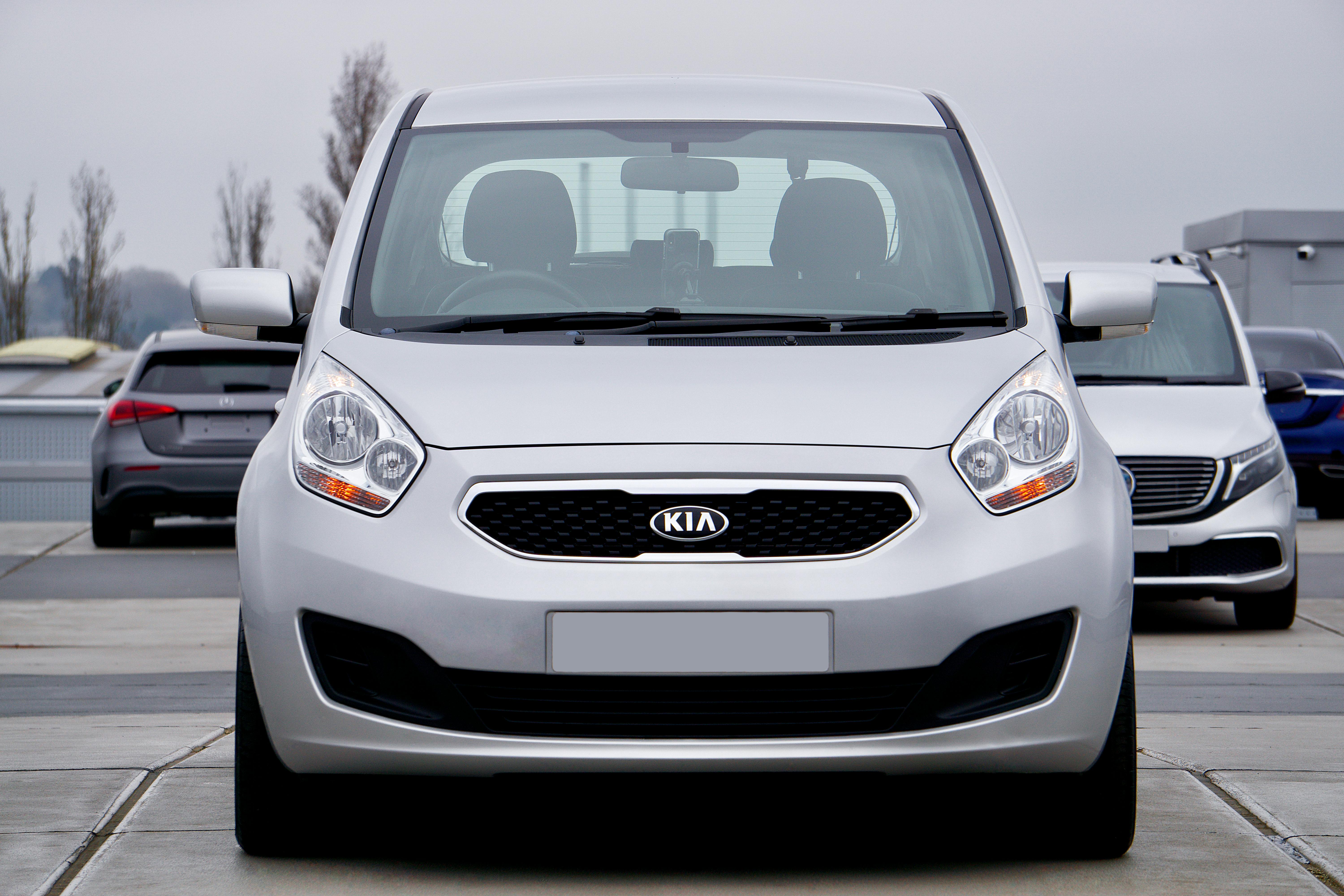 A silver Kia car is parked in a parking lot, captured from the front view.
