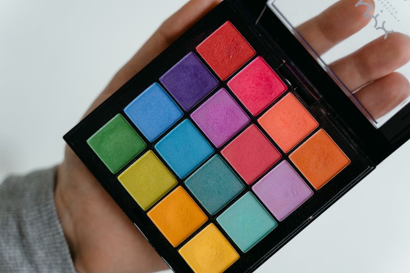Colorful eye shadow palette held in hand, showcasing various shades.