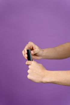 Minimalist photo of a hand holding black lipstick against a purple background.