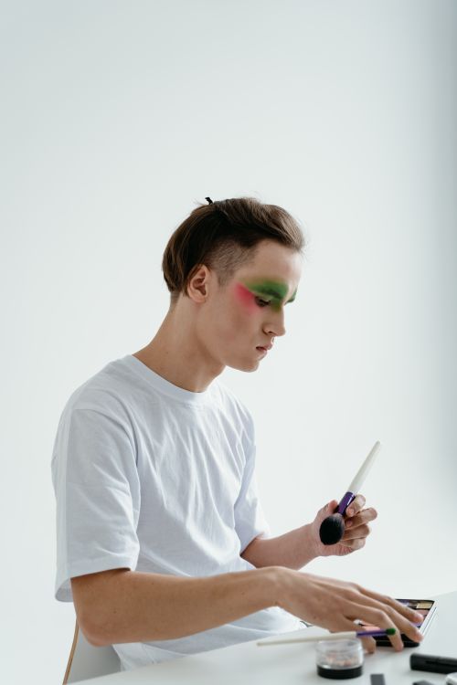Free Young man using makeup brush to apply colorful eyeshadow in an indoor setting. Stock Photo