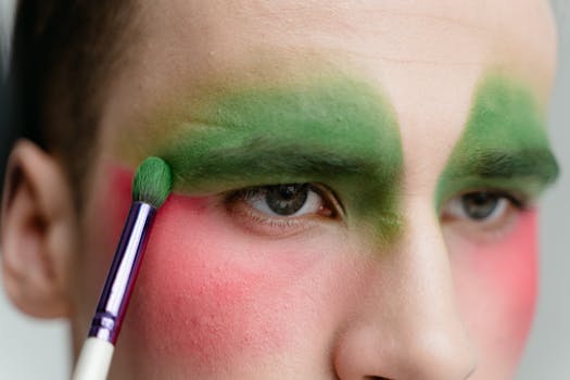Close-up of a model applying bold green and pink eyeshadow with a brush.