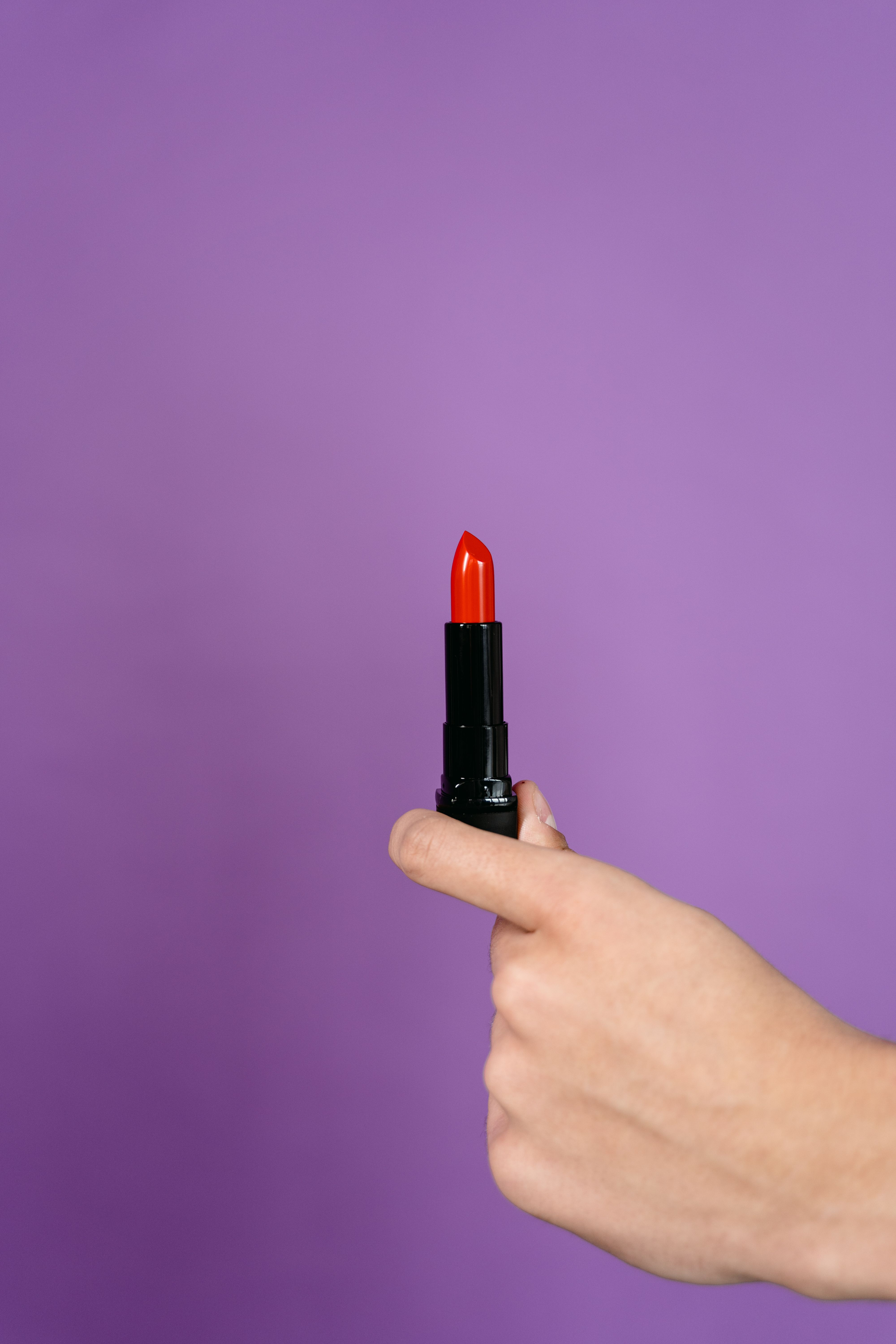 A hand holds vibrant red lipstick with a purple background, perfect for makeup and fashion themes.