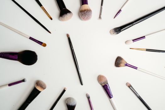 Flat lay of various makeup brushes arranged in a circle on white background.