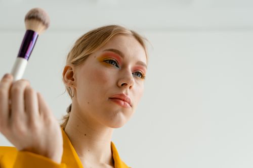 Free Close-up of woman applying vibrant makeup with a brush, featuring colorful eyeshadow. Stock Photo