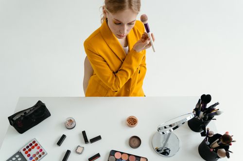Free A woman in a yellow blazer applying makeup at a stylish vanity setup. Stock Photo