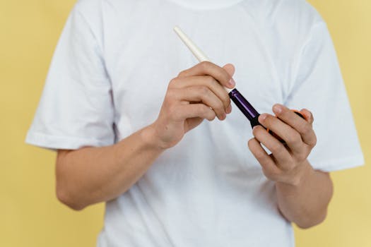 Hands holding a makeup brush against a yellow background. White shirt visible.