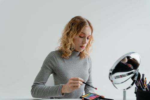 Free Woman using eyeshadow palette at a vanity mirror applying makeup with a brush. Stock Photo