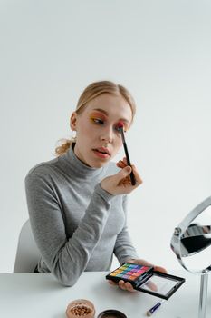 A young woman applies colorful eyeshadow in a cozy indoor setting, promoting beauty and self-expression.