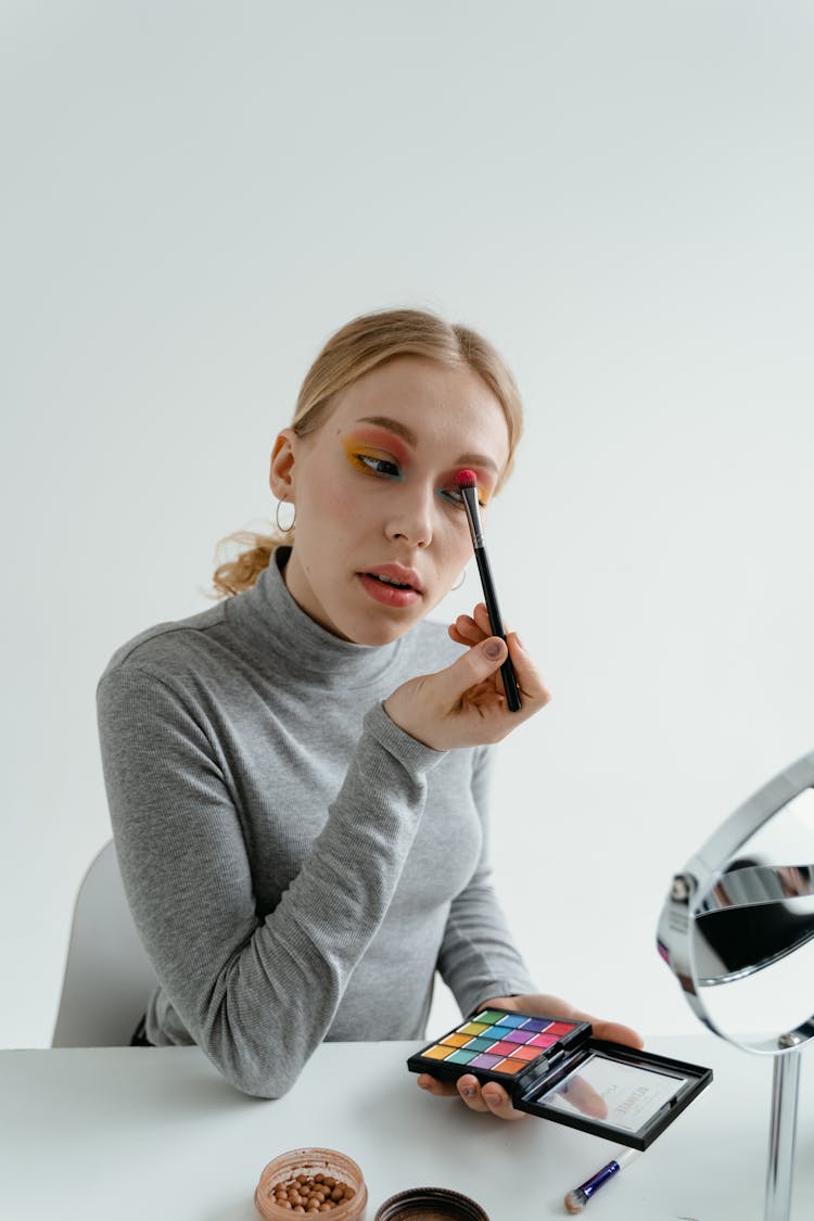 Woman Looking At The Mirror Applying Eyeshadow