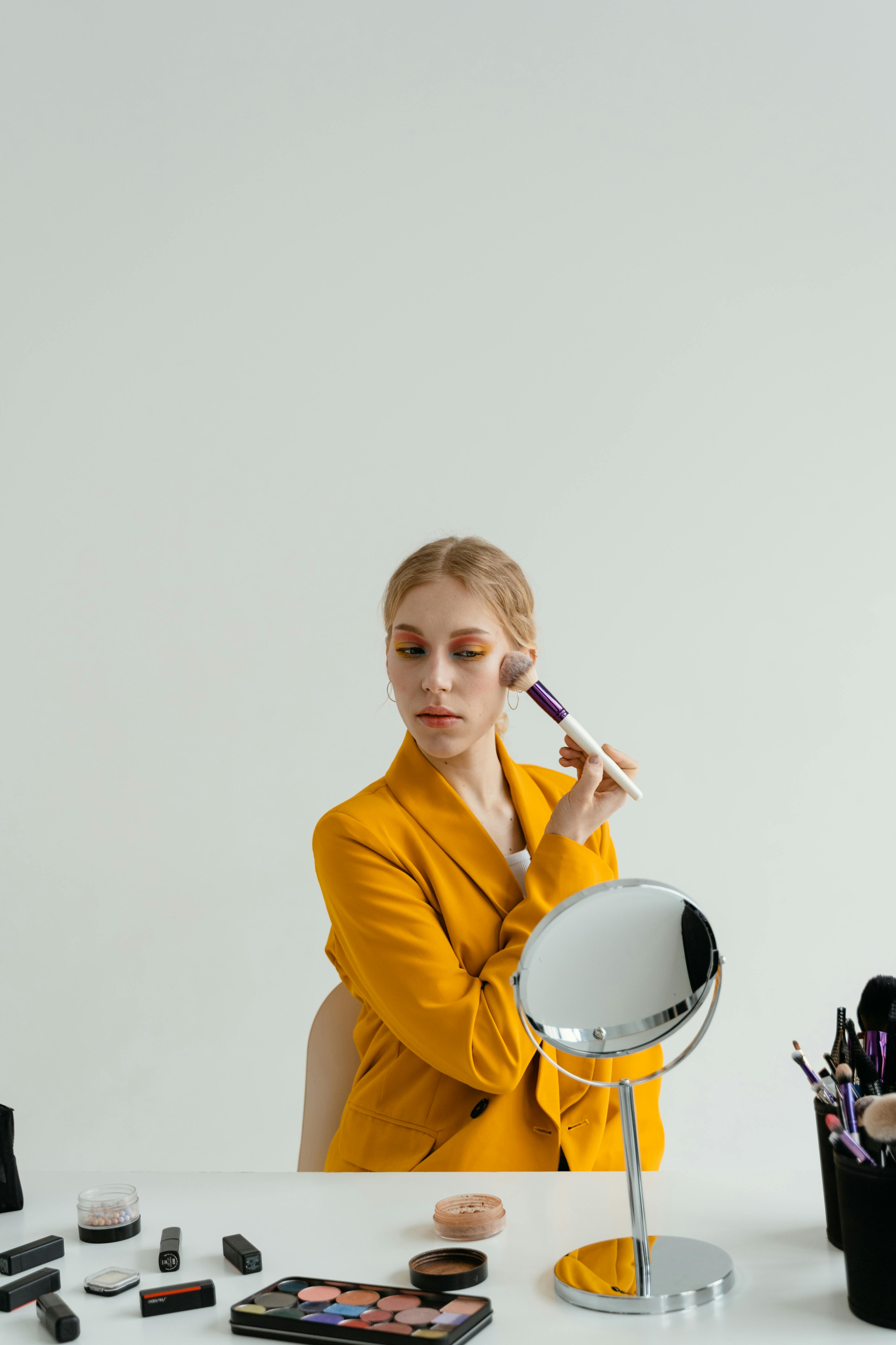 woman in yellow blazer applying makeup