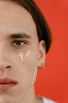 Half face portrait of a young adult with concealer on cheek, vibrant orange background.