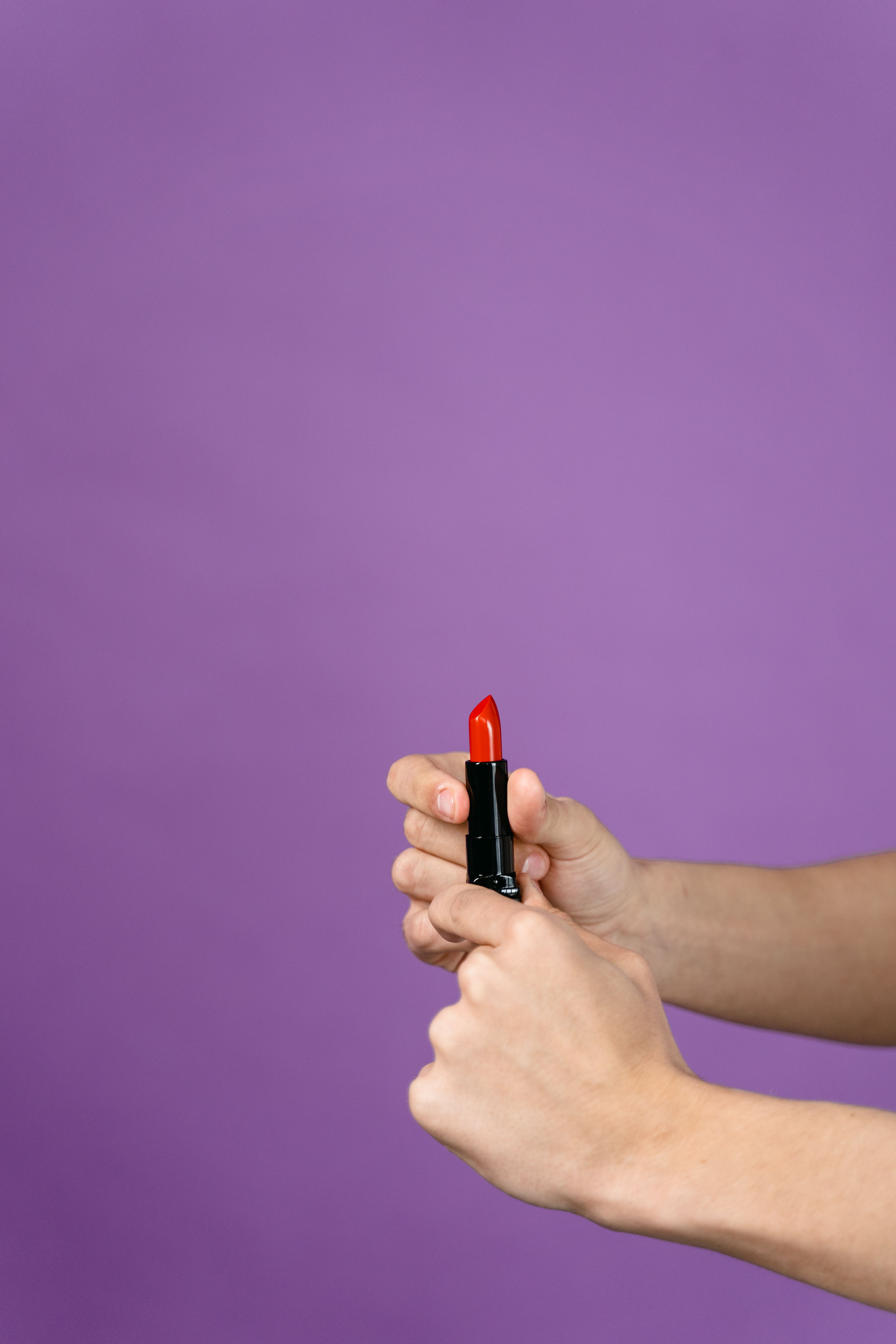 Close-up shot of hands holding a red lipstick against a vibrant purple background.