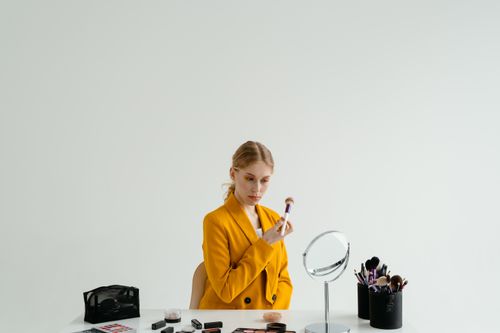 Free Woman in yellow blazer applying makeup at a minimalist dressing table. Stock Photo