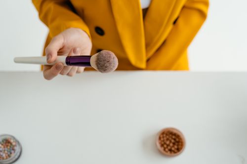 Free A hand holding a makeup brush over a table with cosmetics, featuring a yellow jacket. Stock Photo